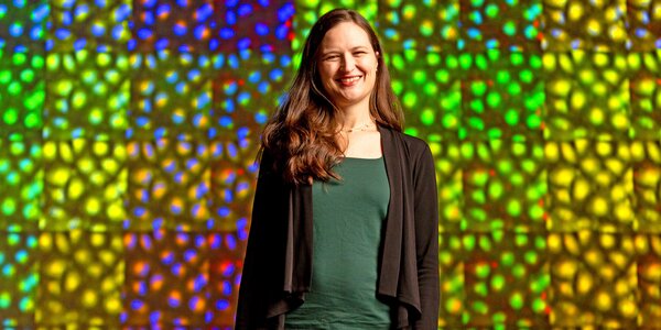 Anne Carpenter smiles for photo against multi-colored bright backdrop of microscopy imagery.